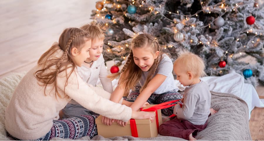 Siblings opening a present near a Christmas tree.